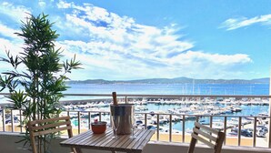 A wooden table with chairs on a balcony overlooking a marina with boats and a clear blue sky. - 4-person apartment facing the sea 50m from the beach and town center (Sainte-Maxime)