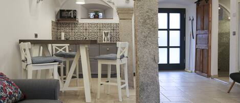 A kitchen with a bar area, white chairs, and a stone column.