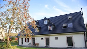 A two-story house with a dark roof, white exterior walls, and a small front porch with a bench. - Live like in a castle, in the vaulted room, rental after complete renovation (Grafengehaig)