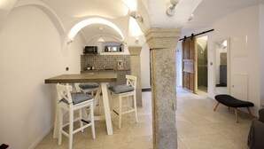A modern kitchen with white walls, a wooden island, and two white chairs with patterned cushions. - Live like in a castle, in the vaulted room, rental after complete renovation (Grafengehaig)