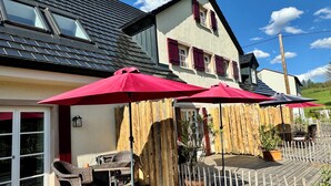 A wooden deck with outdoor furniture and umbrellas, a wooden fence, and a building with a sloped roof and windows. - Live like in a castle, in the vaulted room, rental after complete renovation (Grafengehaig)