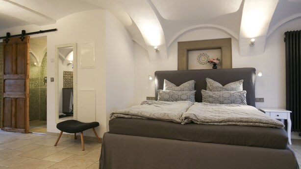A bedroom with a large bed, a small bedside table, and a sliding door leading to a bathroom. - Live like in a castle, in the vaulted room, rental after complete renovation (Grafengehaig)