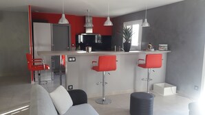 A modern living room with a grey sofa, red bar stools, and a black ottoman. - Detached villa, Swimming pool, Spa, Garden furniture. Near Vallon Pont d'Arc. (Labastide-de-Virac)