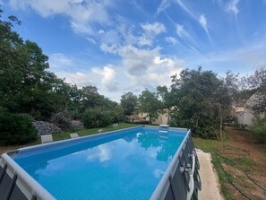An outdoor swimming pool with a clear blue water surface, surrounded by lush greenery and trees.