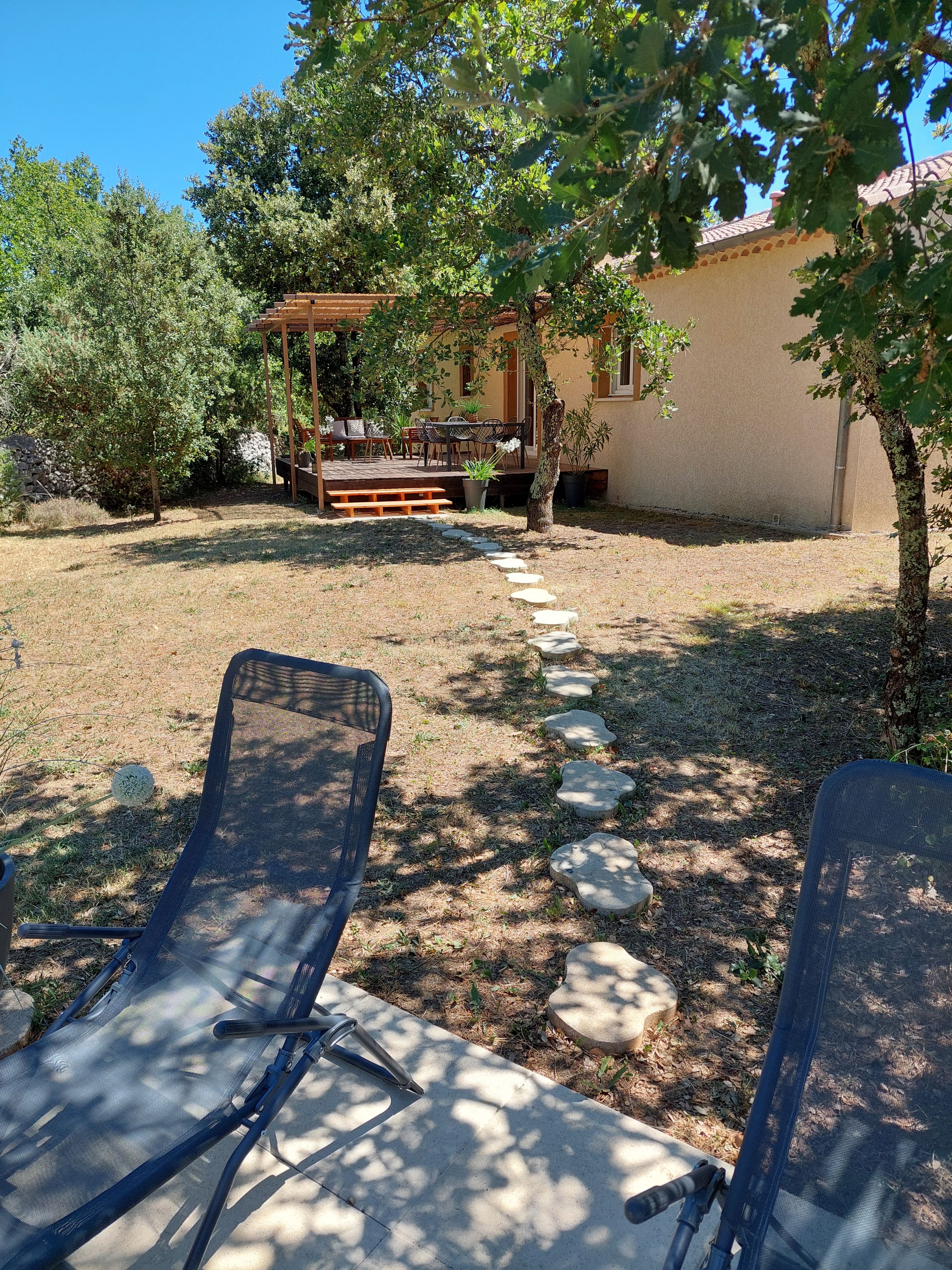 Eine Terrasse mit Gartenmöbeln, einer Pergola und einem Steinweg, der zu einem Gebäude führt.