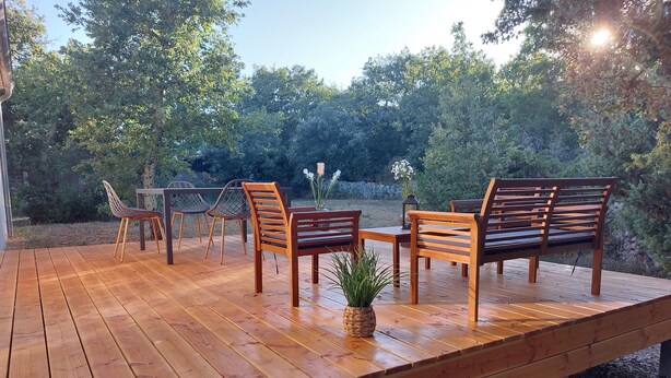 An outdoor wooden deck with a table and chairs, surrounded by trees. - Detached villa, Swimming pool, Spa, Garden furniture. Near Vallon Pont d'Arc. (Labastide-de-Virac)