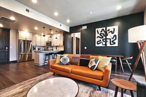 A modern kitchen with stainless steel appliances, a dining area with a dark wall and abstract art, and a cozy living space with a leather sofa and a marble coffee table.