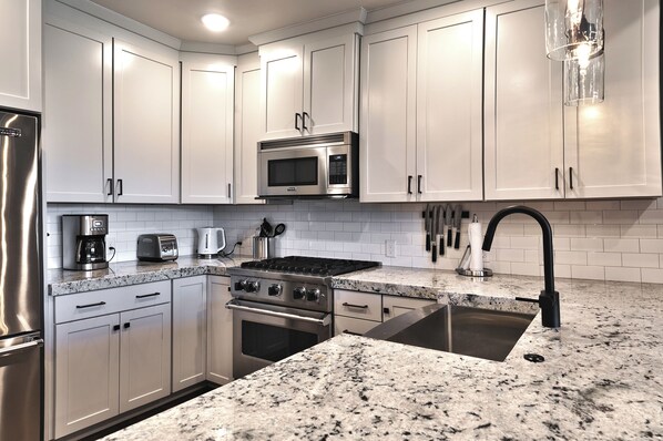 A modern kitchen with white cabinets, stainless steel appliances, a granite countertop, and a black faucet.
