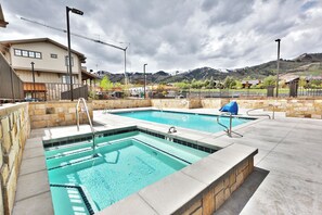 A swimming pool area with two pools, stone walls, and a view of mountains in the background.