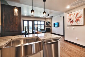 A modern kitchen with granite countertops, stainless steel appliances, pendant lighting, and a large window.