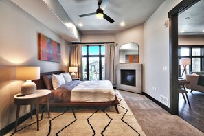 A modern bedroom with a large bed, bedside lamps, a ceiling fan, and a view of the outside through the window.