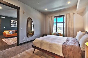Un dormitorio moderno con una cama grande, una zona de estar con sofá y vistas al exterior a través de una ventana.