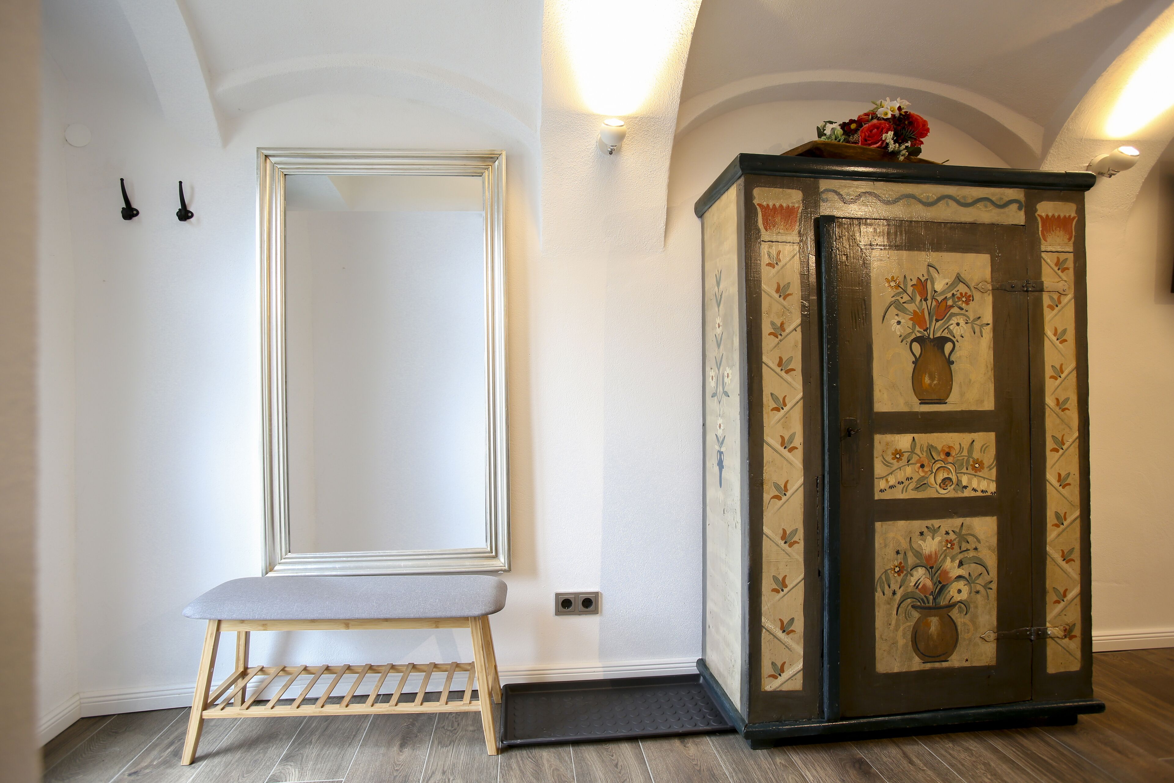 Et værelse med en bænk, et skab med blomstermotiver og en dør med et spejl.