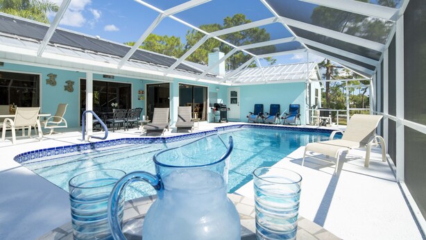 Ein Poolbereich mit Liegestühlen, einer überdachten Terrasse und einem strahlend blauen Himmel.