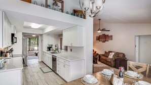 Eine moderne Küche mit weißen Schränken, ein Essbereich mit einem Holztisch für sechs Personen und ein Wohnzimmer mit einer braunen Ledersofa.