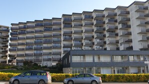 Un immeuble résidentiel à plusieurs étages, doté de balcons, avec une enseigne indiquant « CENTRE-VILLE », et des voitures garées au premier plan.