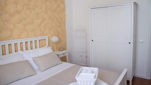 A bedroom with a bed, a nightstand, a lamp, a wardrobe, and a laundry basket. - CAMERA MATRIMONIALE PANORMOS PIENO CENTRO STORICO (Palermo)