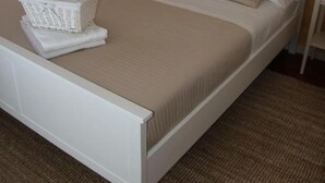 A neatly made bed with a white headboard, beige bedding, and a white basket on the footboard. - CAMERA MATRIMONIALE PANORMOS PIENO CENTRO STORICO (Palermo)