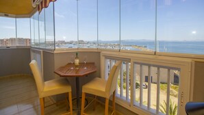 Un balcón con mesa y sillas, con vistas a la costa, edificios y un puerto deportivo.