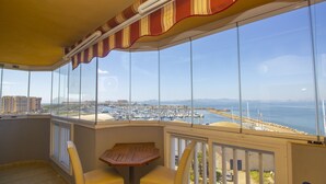 Un balcón con vista a un puerto deportivo y una playa, con una mesa y dos sillas.