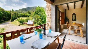 A dining area with a table set for two, overlooking a scenic landscape with hills and trees. - Loft Apt | Mountain Views | Luxury Bath | Forest (Sales De Llierca)