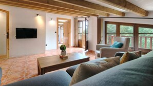 A spacious living room with a wooden ceiling, a television mounted on the wall, a sofa, a chair, and a coffee table. - Loft Apt | Mountain Views | Luxury Bath | Forest (Sales De Llierca)