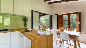 A modern kitchen with a wooden island, white cabinets, and a dining area with a wooden table and chairs. - Loft Apt | Mountain Views | Luxury Bath | Forest (Sales De Llierca)
