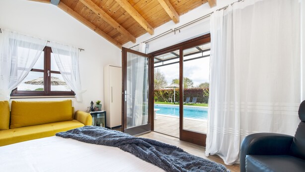 A bedroom with a bed, a yellow sofa, a black armchair, and a sliding glass door leading to a pool area. - House 2041/31790 (Istria - Rovinj), 1000m from the beach (Rovinj)
