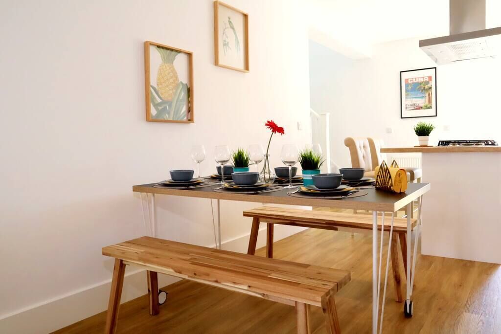 Un coin repas avec une table en bois dressée pour quatre personnes, un banc et un comptoir de cuisine agrémenté d’une plante et d’une affiche.