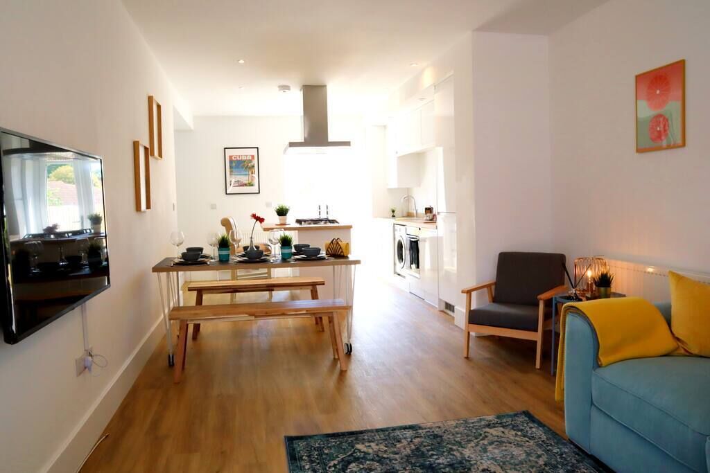 A modern living room with a flat-screen TV, a wooden bench, a blue sofa, and a kitchen in the background.