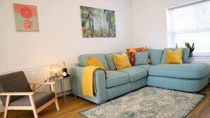 A living room with a light blue sofa, a wooden chair, a patterned rug, and two wall art pieces. - NEW Poole House 5 mins to Sandbanks +Netflix (Poole)