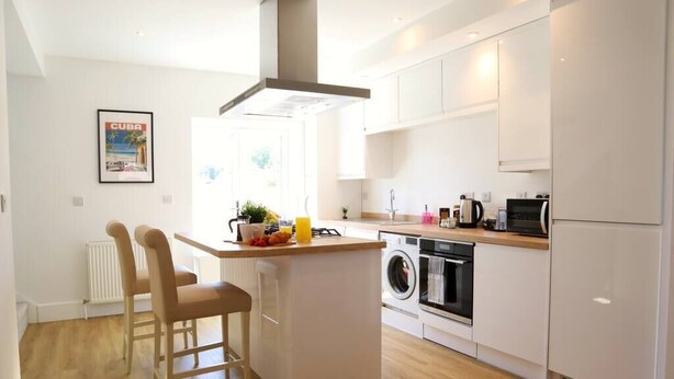 A modern kitchen with a central island, a built-in washing machine, and a dining area with two chairs. - NEW Poole House 5 mins to Sandbanks +Netflix (Poole)