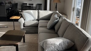 Ein Wohnzimmer mit grauem Sofa, einem Holztisch und einem Essbereich mit Stühlen und Tisch.