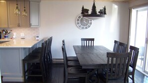 Ein Essbereich mit Holztisch und -stühlen, einer Wanduhr und einer Küchenzeile mit Schränken und Pendelleuchten.