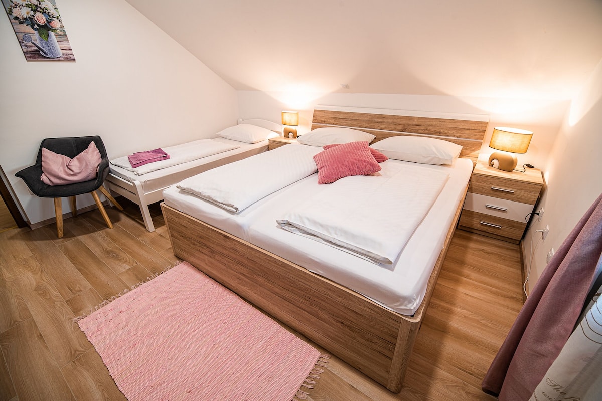 Un dormitorio con dos camas, una silla, una mesita de noche y una lámpara de pared.