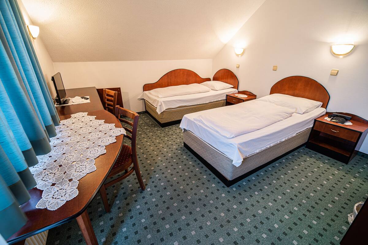 Una habitación de hotel con dos camas, un escritorio con ordenador, una silla y una mesa con mantel de encaje.