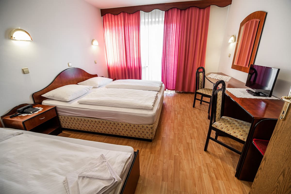 Habitación de hotel con dos camas, un escritorio con silla, un televisor y una ventana con cortinas.