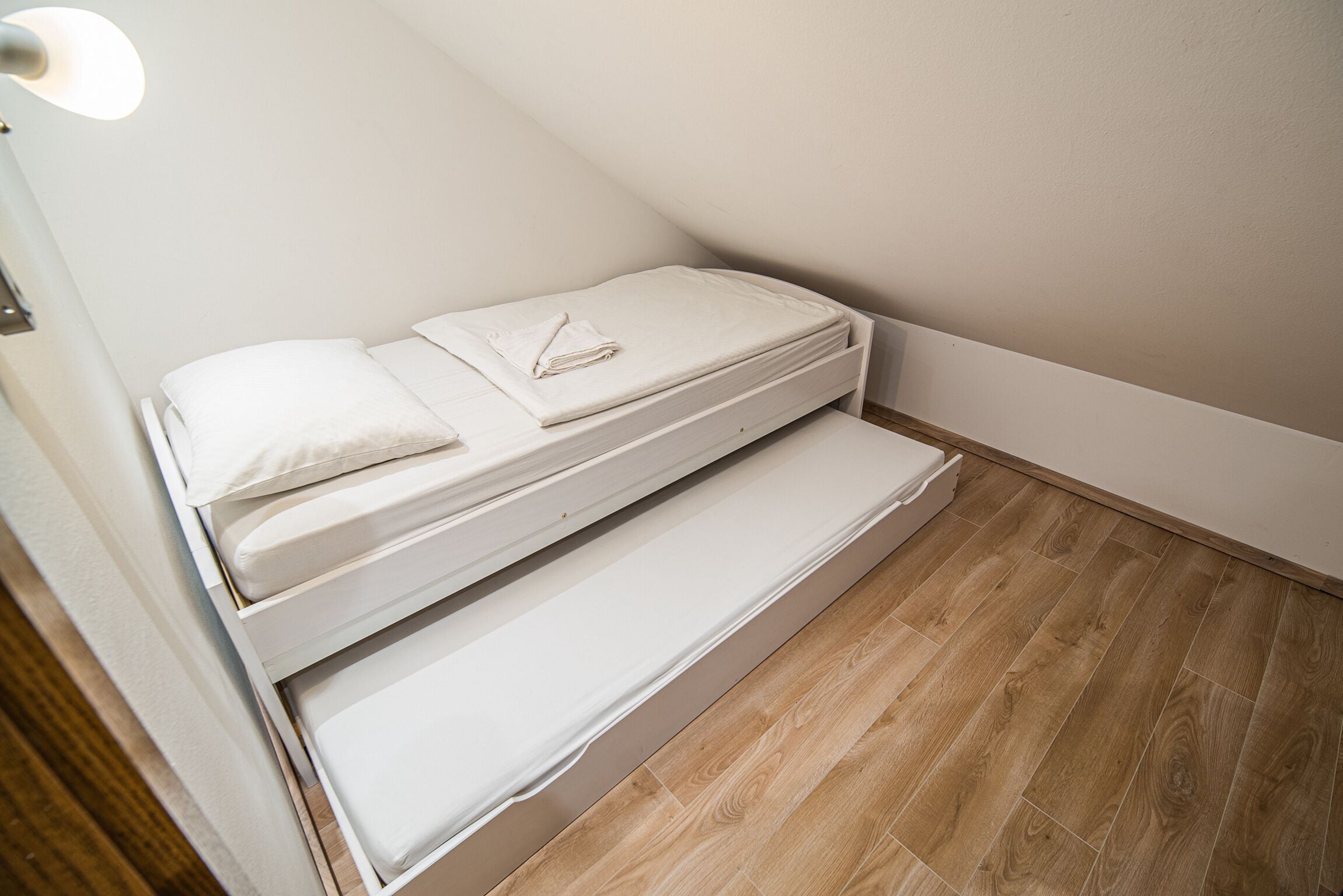Ein kleines Zimmer mit einem Einzelbett, Holzboden und weißen Wänden.