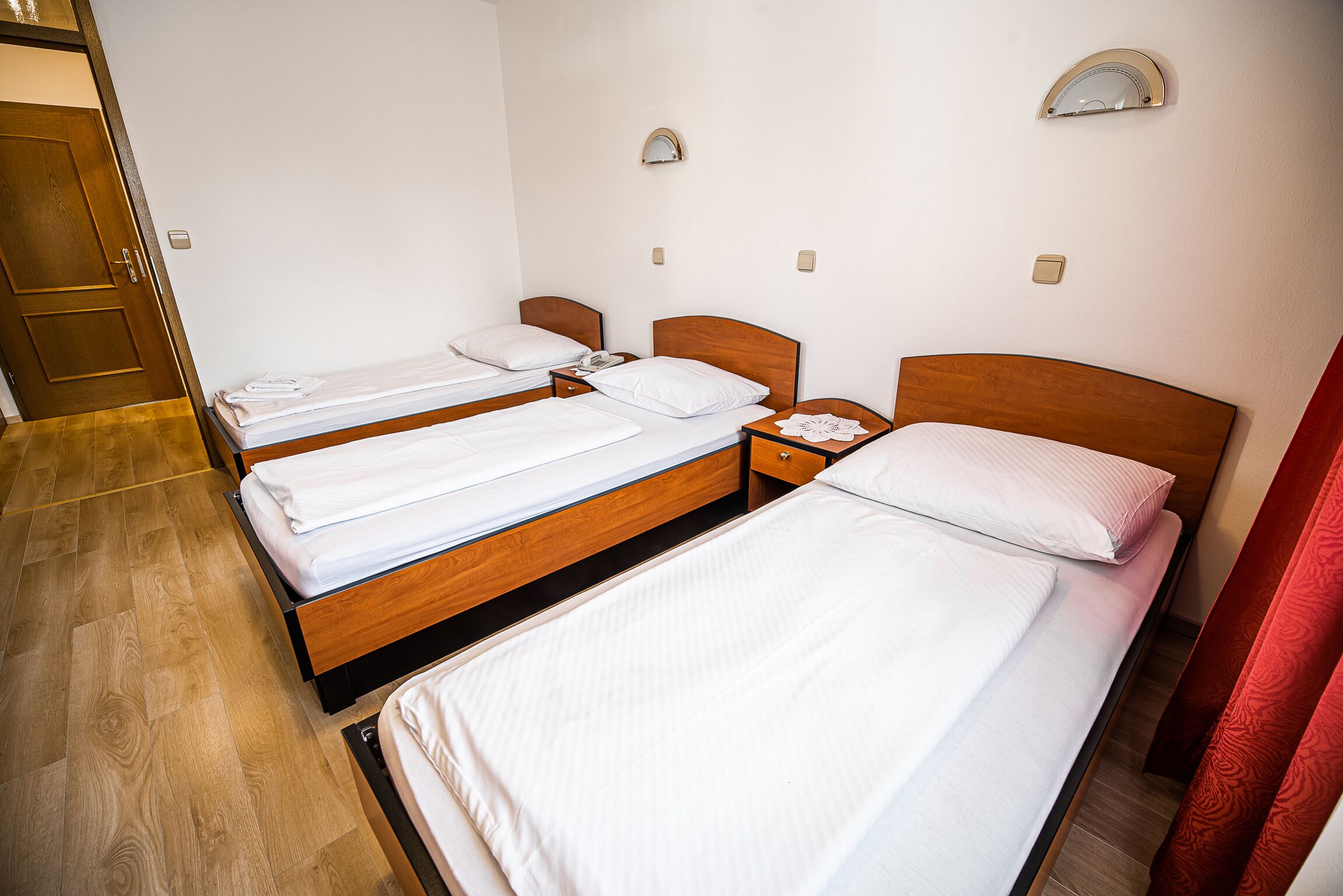 Habitación de hotel con tres camas individuales, cabeceras de madera, ropa de cama blanca, mesitas de noche con lámparas y suelo de madera.