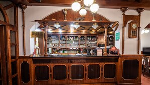 Una zona de bar con armarios de madera, estantes llenos de botellas y un reloj en la pared.