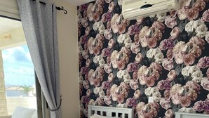A bedroom with two beds, a window with curtains, a wall-mounted air conditioner, and a floral wallpaper. - Villa Denis, heated pool on request, centrally located in Coral Bay (Coral Bay)