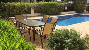 A poolside area with a table and chairs, surrounded by greenery and a tiled pool. - Villa Denis, heated pool on request, centrally located in Coral Bay (Coral Bay)