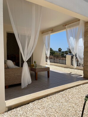 A balcony with a wicker sofa and a glass table, covered by sheer white curtains. - Villa Denis, heated pool on request, centrally located in Coral Bay (Coral Bay)