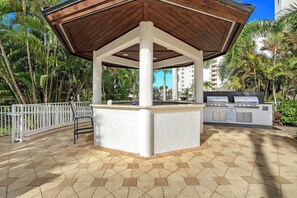 Um pátio externo com um gazebo de madeira, uma estação para churrasco e um cercado branco.
