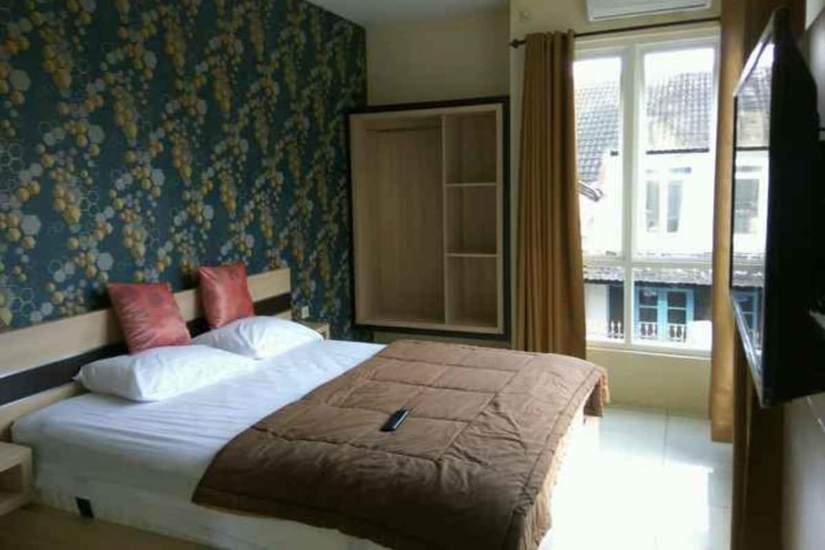 A hotel room with a bed, a wardrobe, a window with curtains, and a TV.