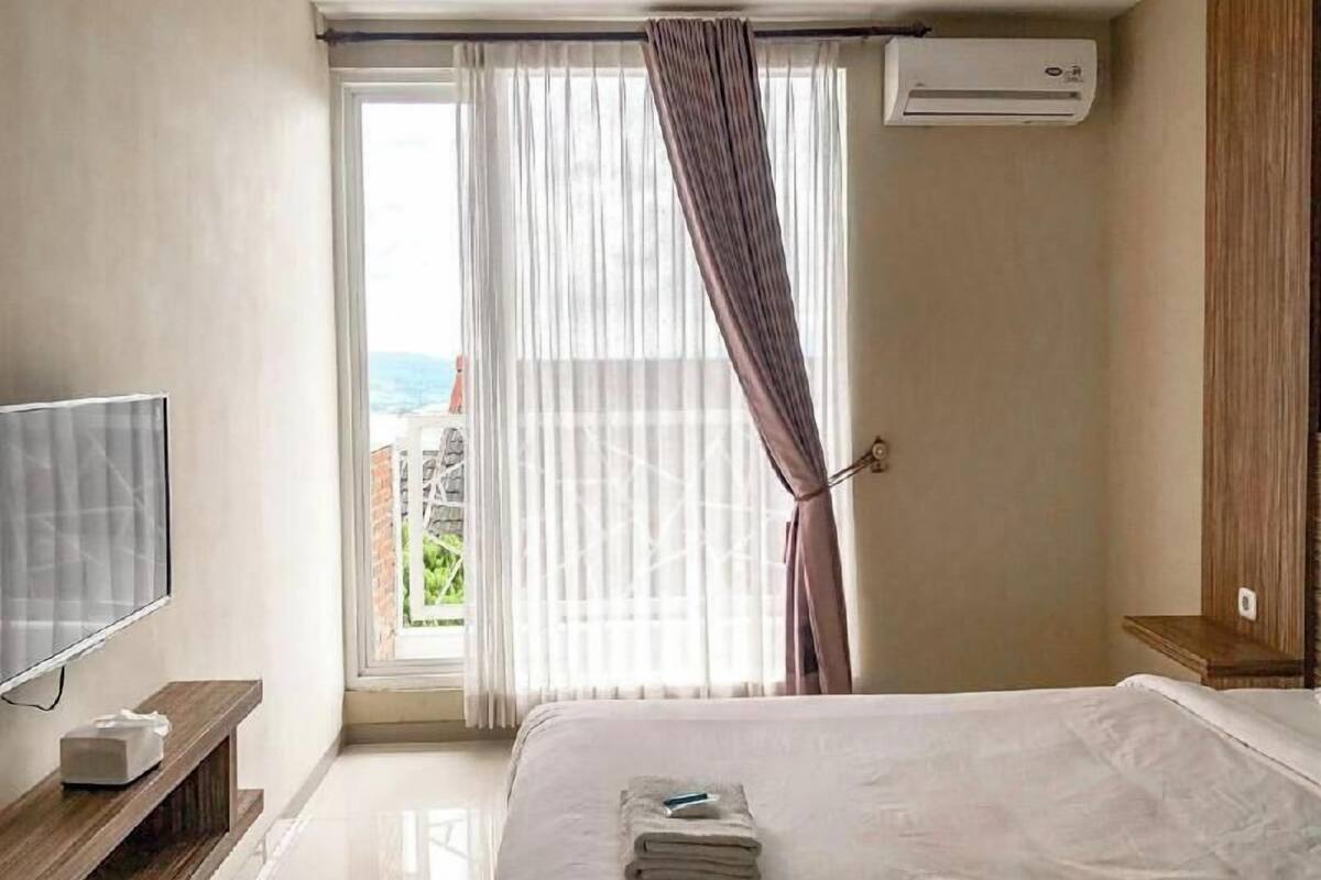 A hotel room with a bed, a TV, an air conditioner, and a view of the outdoors.