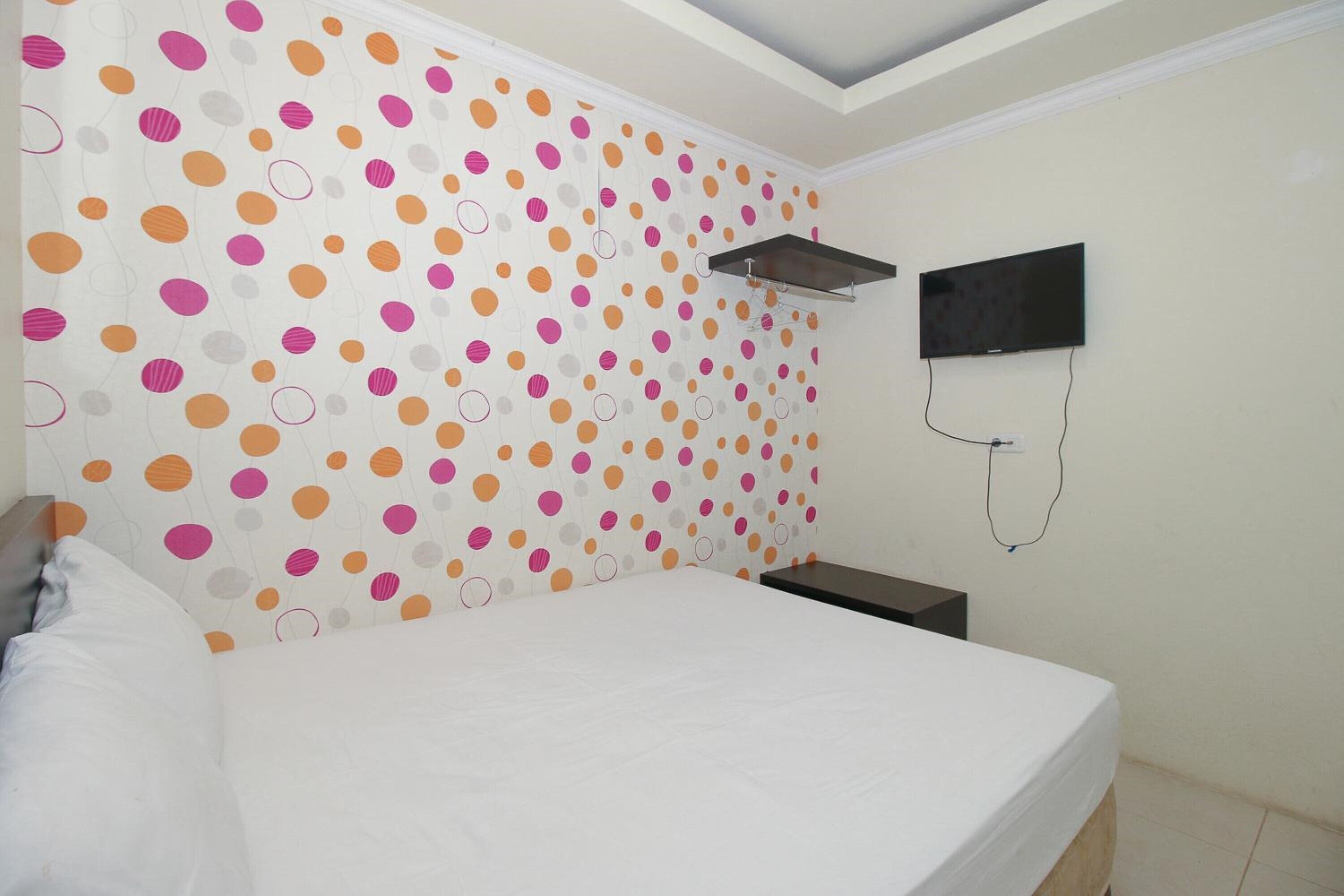 Ein Schlafzimmer mit Punkte-Tapete, einem Bett, einem an der Wand befestigten Fernseher und einem kleinen Tisch.
