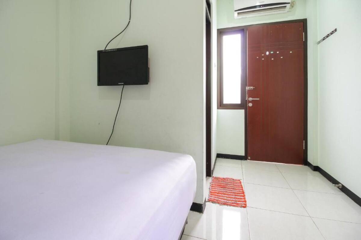 A room with a bed, a flat-screen TV mounted on the wall, a wooden door, and a tiled floor.