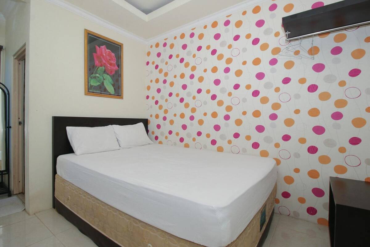 A bedroom with a bed, a painting of roses, and a polka dot wallpaper.