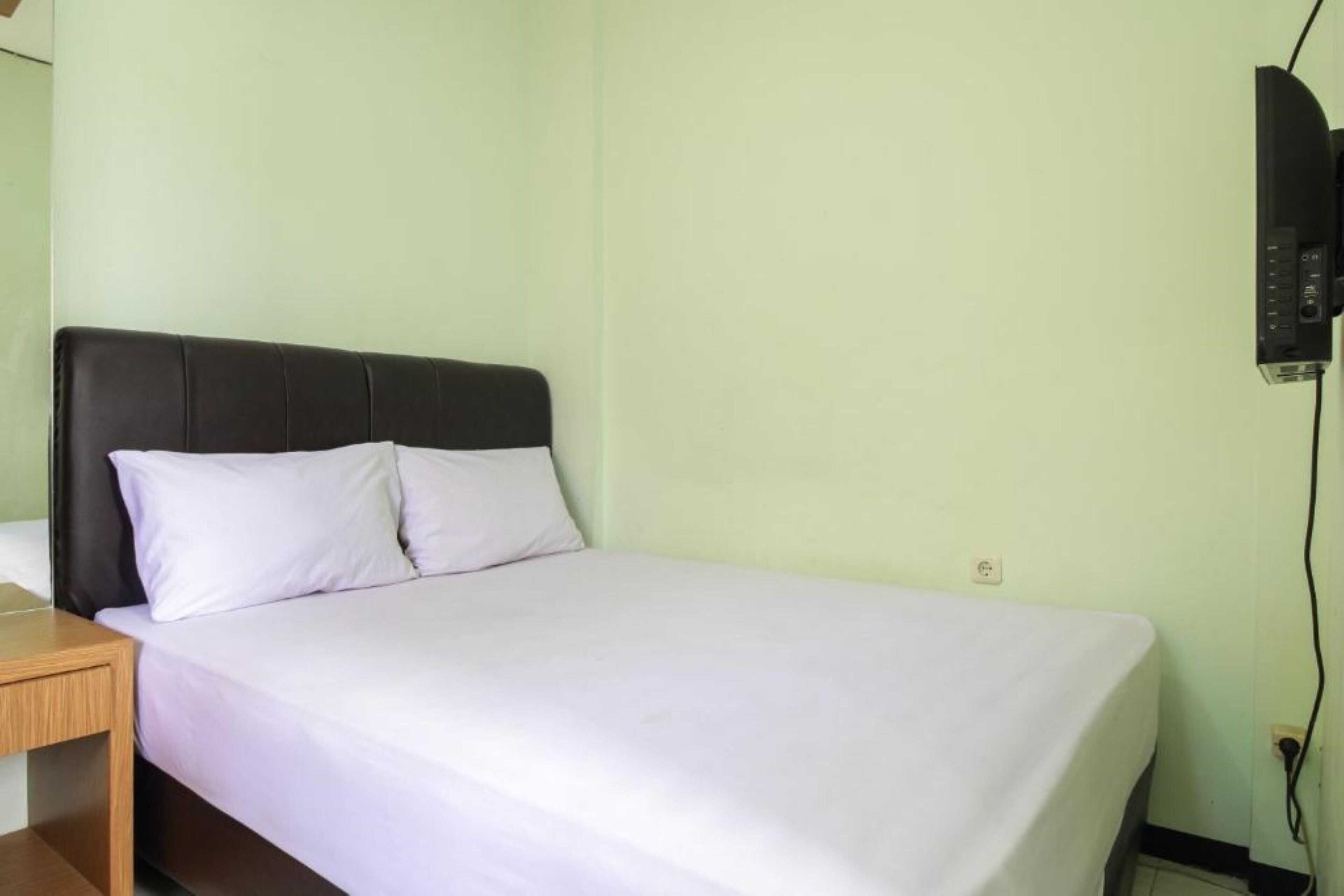 A single bed with a black headboard and white bedding in a room with light green walls.